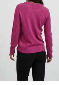 Fuchsiastrumptröja med ribbad nederkant och ärmslut, med en bred halsringning och mjuk textur. Buren med svarta byxor, visad från baksidan.