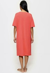 Koronkowa sukienka-t-shirt w kolorze koralowym, z krótkimi rękawami, luźnym krojem i prostym dołem. Wykonana z miękkiego materiału, z okrągłym dekoltem.