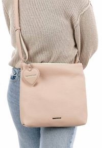 Light pink leather shoulder bag with a textured finish, featuring a heart-shaped charm and a silver logo on the front. Adjustable strap.