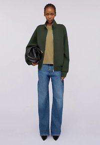 Zelená bomber bunda, olivový top, modré džíny s širokými nohavicemi, černá kabelka, boty na vysokém podpatku, hladká látka, zip na bundě.