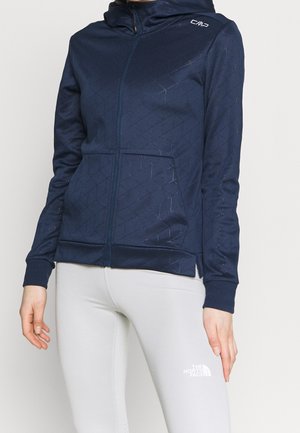 Marinblå zip-up hoodie med ett mönstrat textur, med en huva och elastiska manschetter. Matcher med ljusgrå leggings som visar logotyp.