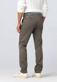 Pantaloni in cotone grigi da uomo con fit dritto, passanti per cintura e due tasche posteriori. Abbinati a sneaker bianche e un maglione bianco strutturato.