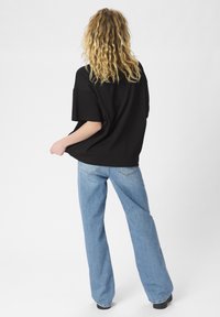 T-shirt nera oversize con maniche corte ampie, abbinata a jeans dritti blu chiaro. Tessuto morbido con una vestibilità rilassata.