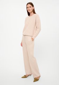 Maglione rosa chiaro a trama con scollatura rotonda, abbinato a pantaloni beige a gamba larga e scarpe con tacco a punta verde oliva con fiocchi.