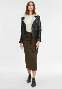 Zwarte leren jas met een schapenvachtkraag, crèmekleurige trui en bruine midi-rok. Opvallende zwarte enkellaarsjes met gespen. Soepele texturen.