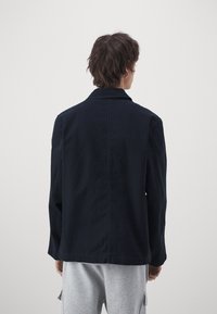 Chaqueta azul marino con cuello y mangas largas, con un corte holgado. Hecha de una tela sólida, textura lisa, sin patrones ni adornos visibles.