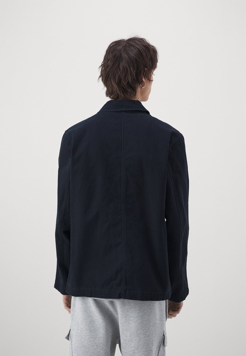 Chaqueta azul marino con cuello y mangas largas, con un corte holgado. Hecha de una tela sólida, textura lisa, sin patrones ni adornos visibles.