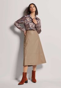 Lange beige leren rok gecombineerd met een gestreepte bruine zijde blouse en roestkleurige enkellaarsjes met hak en ritssluiting.