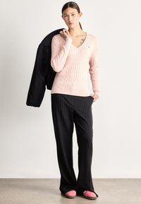 Gaiši rozā adīts džemperis ar V-veida izgriezumu, kopā ar tumšām biksēm ar platu kāju un svītrainu rakstu. Melna jaka uzmestā plecā un rozā apavi.