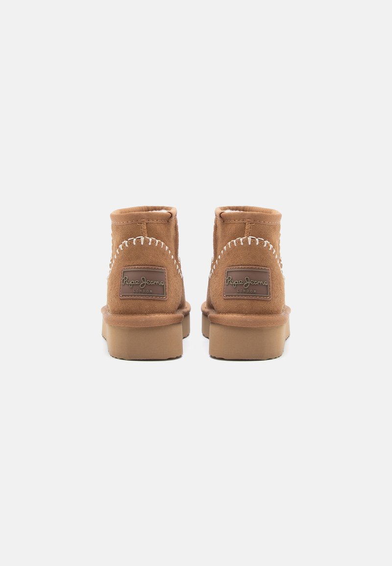 Bottines en suede marron à bout arrondi, avec des accents de couture blanche et une semelle en caoutchouc. Présente un logo sur le panneau arrière.