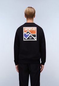 Sort sweatshirt med et grafisk design på ryggen, der viser bjerge i orange, blå og hvid, samt "NAPAPIJRI 87" nedenfor.