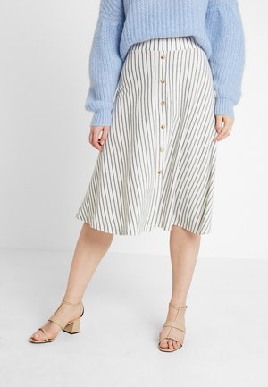 Woman wearing a white and black vertical striped button-front skirt, light blue knit sweater, and beige heeled sandals.