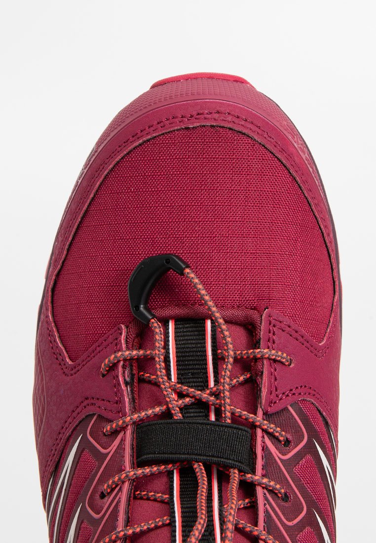 Scarpa sportiva rossa con tomaia in tessuto testurizzato, accenti neri e bianchi, e un sistema di allacciatura sicuro. Punta rinforzata e imbottitura visibile.