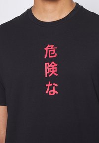 Czarny bawełniany t-shirt z okrągłym dekoltem, z wyraźnym, pionowym czerwonym napisem w japońskich znakach z przodu. Gładka tekstura.