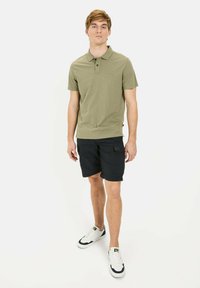 Oliven grøn polo skjorte med et lille logo, parret med sorte cargo shorts. Modellen bærer hvide sneakers med sorte akcenter. Simpelt, afslappet design.