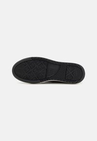 Black rubber shoe sole with distinct herringbone pattern, featuring a central logo area and smooth, rounded toe design.