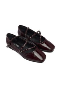 Chaussures plates en cuir verni bourgogne avec embouts carrés, brides croisées ornées de petits clous ronds, et une finition lisse et brillante.