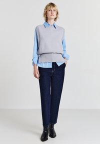 Gilet grigio a maglia su una camicia azzurro chiaro con bottoni, abbinato a jeans in denim scuri e stivaletti neri alla caviglia. Design semplice e moderno.