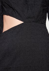 Schwarzes Texturkleid mit Ausschnitt im Taillenbereich, aus gekrepptem Stoff mit dezentem Glanz.