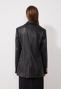 Veste en cuir noir avec une silhouette structurée, ornée de boutons dorés aux poignets et d'une finition lisse et brillante.