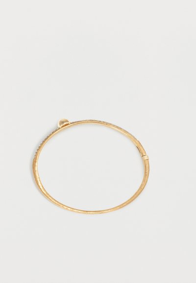 Λεπτό βραχιόλι σε χρυσό χρώμα με μεταλλική επιφάνεια με υφή και μικρό κλείστρο σε απλό φωτεινό φόντο.