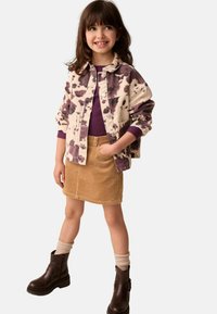 Giacca tie-dye lilla e crema, camicia viola scuro, gonna in velluto a coste color sabbia, stivaletti marroni alla caviglia, calze beige. Outfit casual a strati.