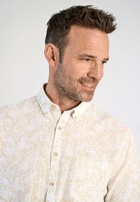 Camicia a maniche corte di colore chiaro con motivo floreale, colletto con bottoni e taschino sul petto, caratterizzata da bottoni in una sfumatura a contrasto leggera.