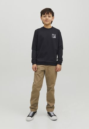 Felpa blu scuro con scollo rotondo, caratterizzata da una piccola stampa grafica. Abbinata a pantaloni beige e sneakers bianco e nere.
