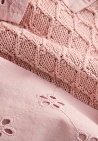 Dżersej w jasnoróżowym kolorze z teksturowanym wzorem w diamenty, nałożony na gładki materiał z haftem kwiatowym i delikatnymi detalami szycia.