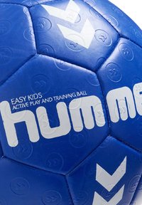 Niebieska, syntetyczna piłka do ręcznej z białymi akcentami i brandingiem, posiadająca fakturowaną powierzchnię i sześciokątne panele dla lepszego uchwytu. Odpowiednia dla dzieci.