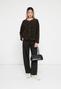 Brown fuzzy jacket, four buttons, brown wide-leg trousers, white sneakers with yellow soles, holding a small black bag.