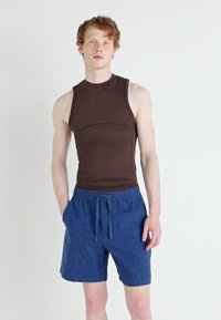 Brun ærmeløs top lavet af glat stof, parret med blå strukturerede shorts med elastisk talje og snørre.