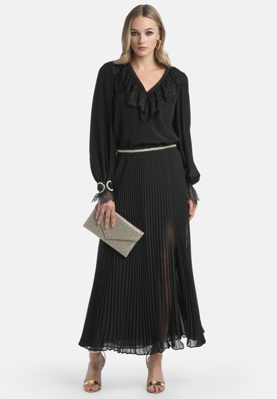 Black blouse with ruffled lace neckline, high-waisted pleated black skirt, glittery silver clutch, and gold heeled sandals.