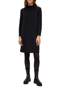 Czarna sukienka z kołnierzem typu cowl, z długimi rękawami, o gładkiej fakturze, w długości do kolan, zestawiona z czarnymi wysokimi botkami i fakturowanymi rajstopami. Prosty fason.