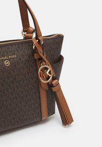 Borsa a tracolla marrone con motivo, dotata di accessori in oro, logo e frangia in pelle. Presenta una chiusura con zip e doppi manici.
