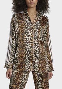 Leopardmönstrad satinpyjamas-set som inkluderar en långärmad skjorta med knappar och vita accentlinjer samt matchande byxor. Slät, glänsande textur.