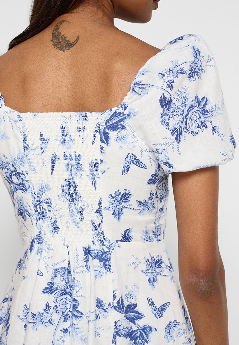 Gesticktes Blümchenkleid in Weiß und Blau, mit Puffärmeln und quadratischer Ausschnitt. Ausgestattet mit einem botanischen Muster und strukturiertem Stoff.