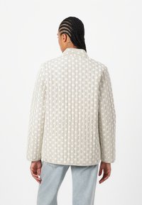 Chaqueta acolchada en blanco roto con un patrón geométrico, que cuenta con un cuello afilado, un corte relajado y detalles de costura visibles.