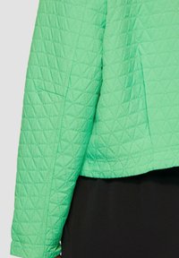 Zelená prešívaná bunda s geometrickým diamantovým vzorom, bočnou kapsou a skráteným strihom, kombinovaná s čiernym topom.