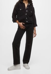 Giacca di jeans nera con un design corto, dotata di due tasche frontali, bottoni argentati e maniche lunghe. Abbinata a pantaloni neri a vita alta e sneakers bianche.