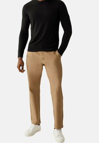 Pantalons chinos couleur sable en coton, dotés d'une coupe slim, de poches latérales et d'une texture lisse, assortis à un haut noir à manches longues et des baskets blanches.