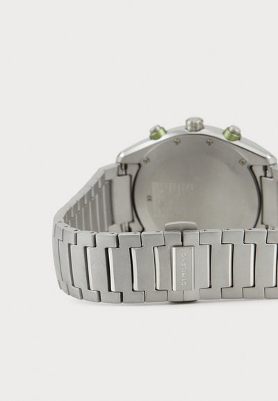 Hõbedane metallkell, millel on mustriga link-randmekäe, ümmargune korpus, rohelised aktsendid kroonil ja poleeritud viimistlus.