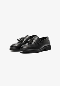 Mocassins en cuir noir avec des détails en pampilles, texture lisse, talon bas et bout arrondi. Présentent des coutures discrètes le long des bords.