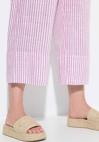 Vaaleanpunaiset ja valkoiset kevyet raidalliset lyhyet housut siistillä helmapäätteellä, yhdistettynä beigeihin kudottuihin liukuviin sandaaleihin, joissa on teksturoitu välipohja.