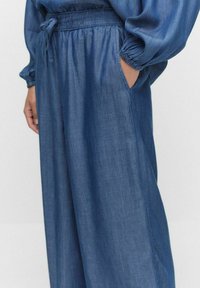 Denimbyxor med vida ben, elastisk midja med dragsko och sidofickor, med en slät, medelmörk blå yta.