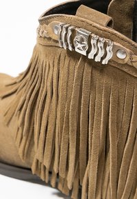 Brązowe zamszowe botki za kostkę z frędzlami i dekoracyjnym srebrnym akcentem w kształcie gwiazdy. Teksturowana powierzchnia, zaokrąglony kształt.