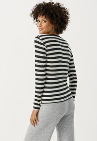 Langärmliges Oberteil in Schwarz und Grau mit gestreiftem Muster und rundem Ausschnitt, kombiniert mit grauen Sweatpants. Weicher Stoff, figurbetontes Design.