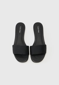 Svarta badsandaler med en bred präglad rem som har en diskret logga och en slät matt yta, designade för avslappnad användning.