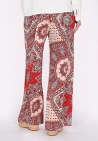 Pantaloni a gamba larga, con motivo in rosso e beige caratterizzati da intricati design paisley, realizzati in un tessuto morbido e con una texture liscia, dotati di vita bassa e taglio a zampa.