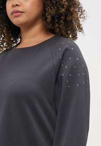 Donkergrijze sweatshirt met een ronde hals en raglanmouwen, voorzien van metalen pailletten op één schouder ter decoratie. Zachte stoftextuur.